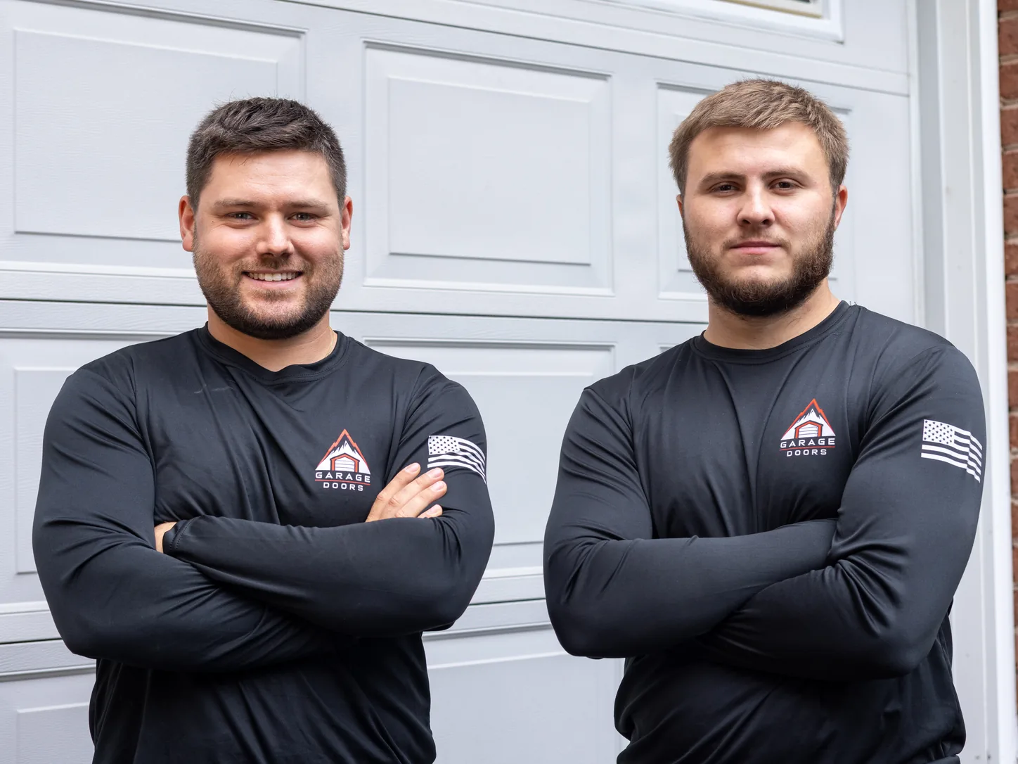 Apex Garage Doors technicians in branded shirts outside a white garage door on a brick home