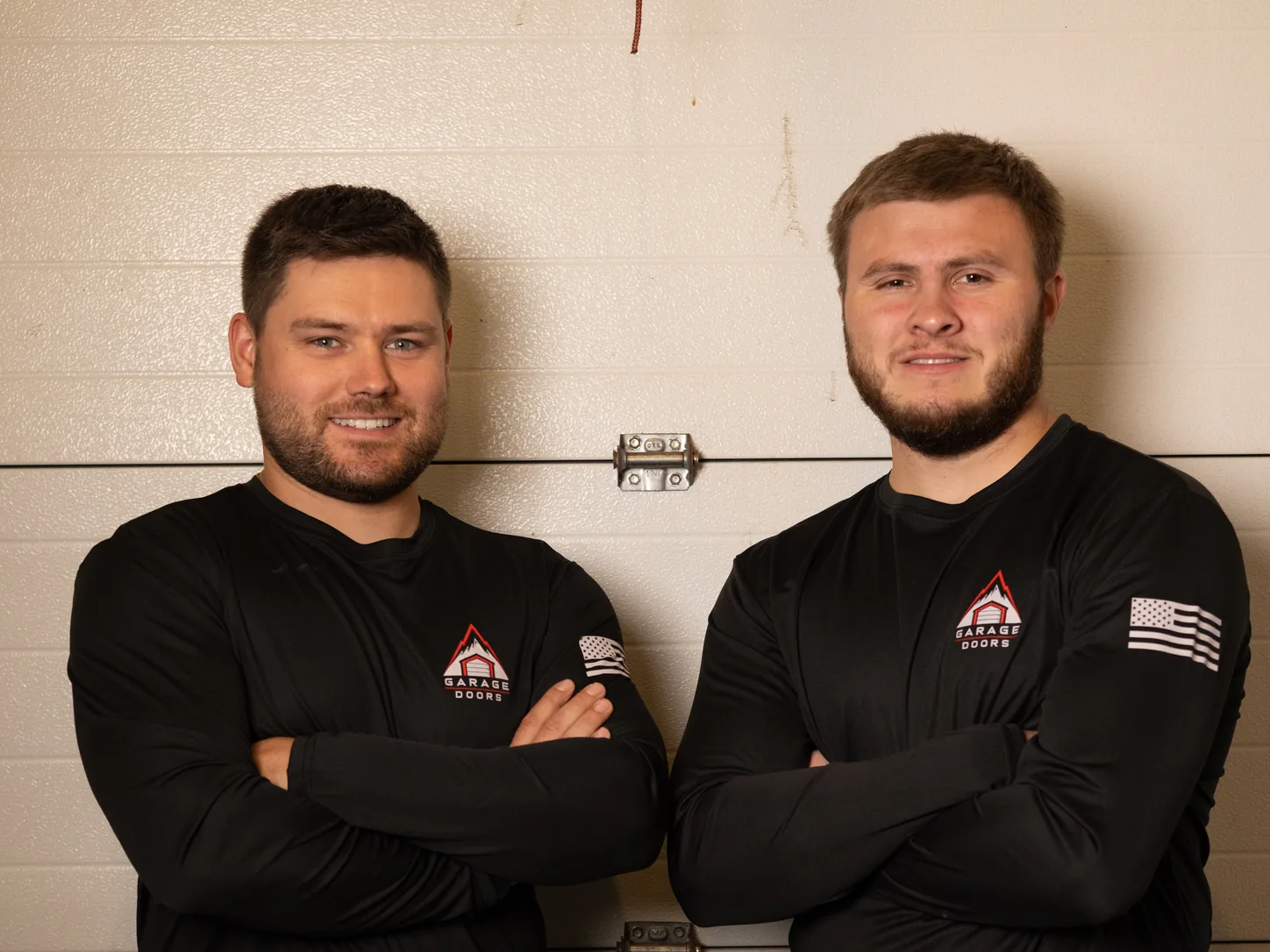 Two Apex Garage Doors technicians with arms crossed inside a garage with a white steel door