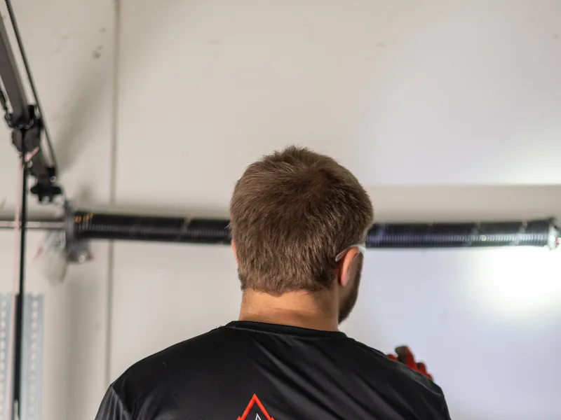 Apex Garage Doors technician in a branded shirt working on a garage door from inside the garage