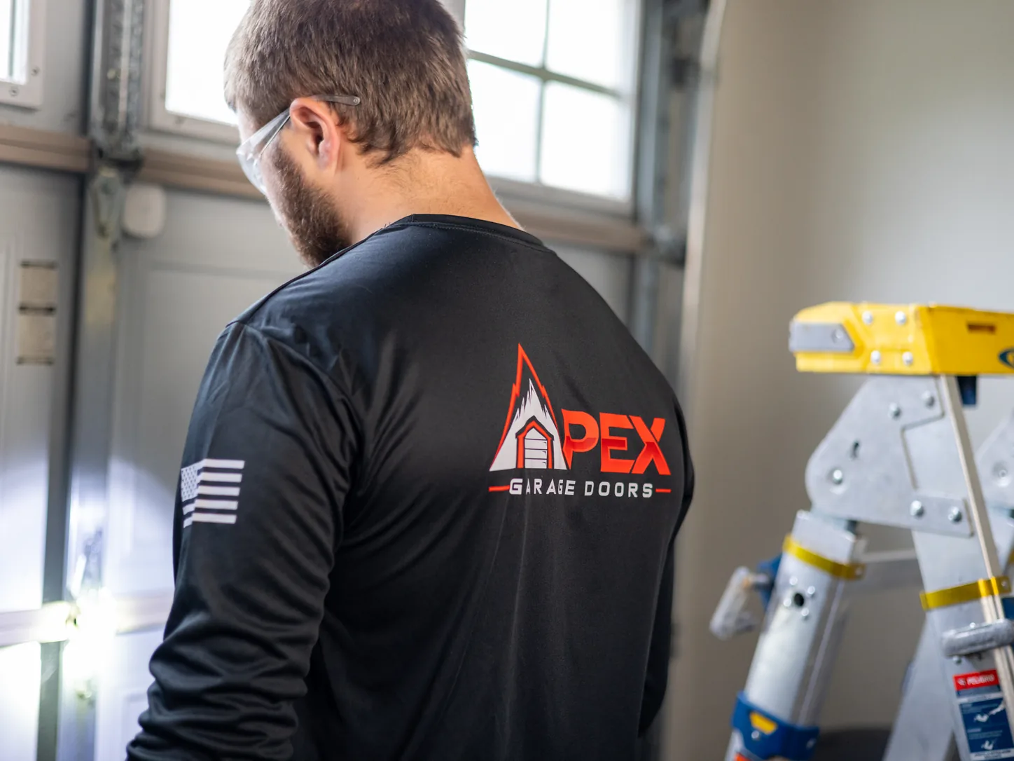 Apex Garage Doors technician in a branded work shirt beside a step ladder on a service call