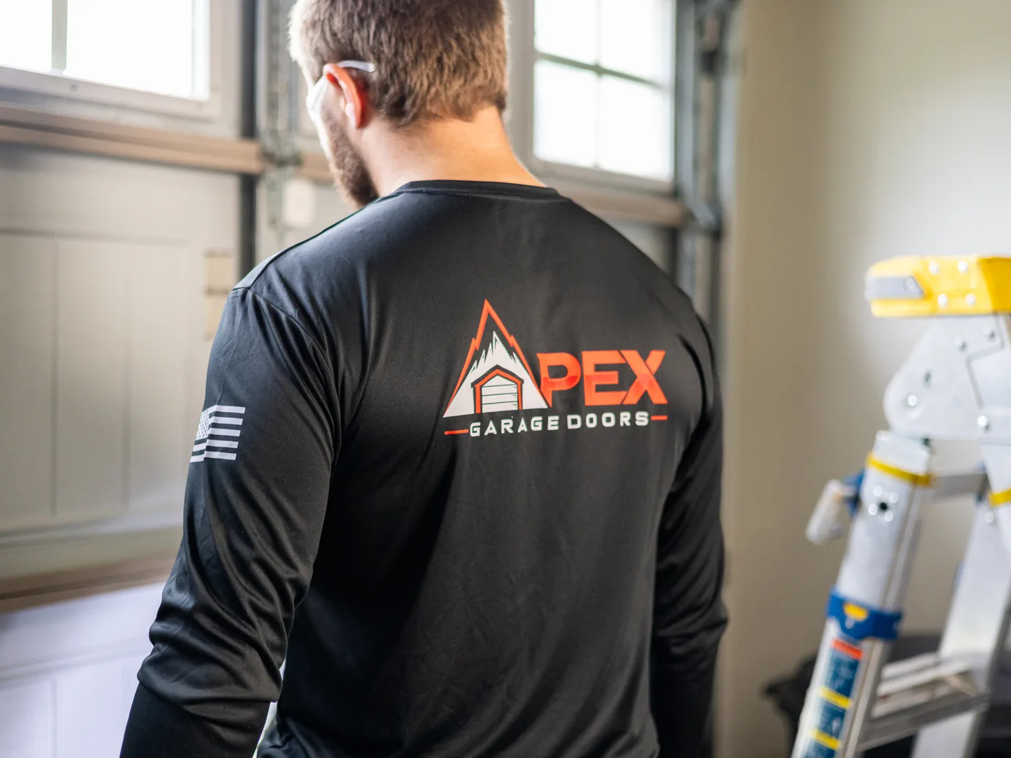 Apex Garage Doors technician on a residential service call with a step ladder in the garage