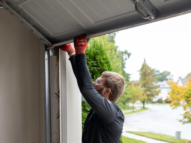 Technician in red work gloves checking a sectional garage door panel from the driveway