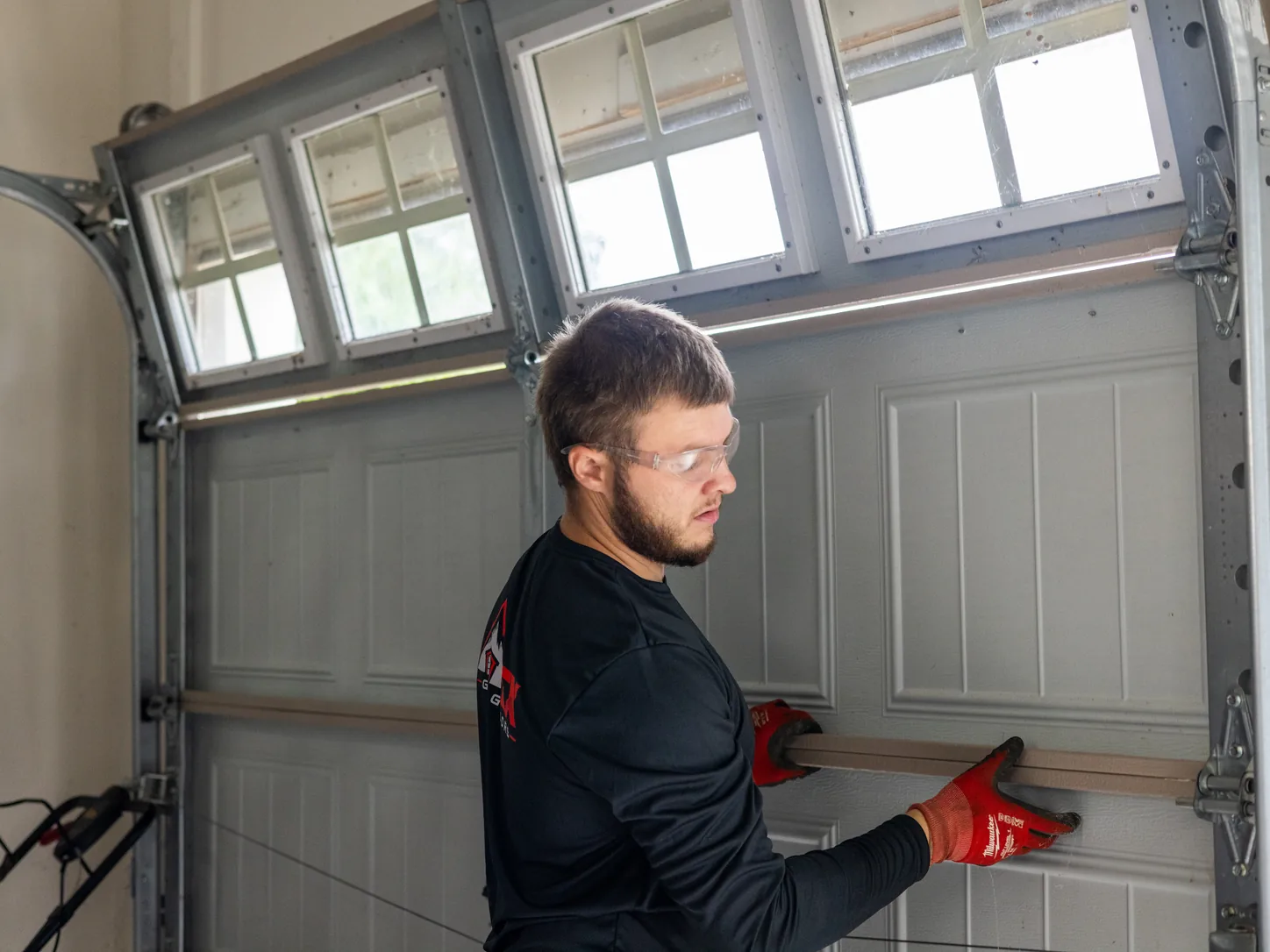 Technician in safety glasses and red gloves checking the panels of a white garage door with windows